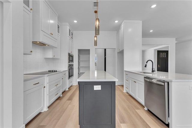 kitchen featuring a kitchen island, light wood-style flooring, appliances with stainless steel finishes, white cabinets, and a sink