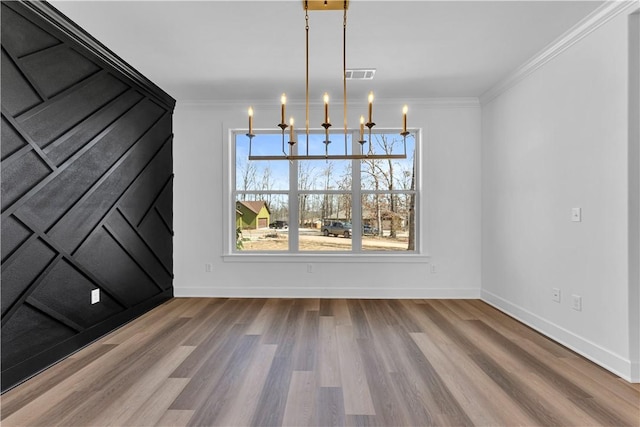 unfurnished dining area with visible vents, wood finished floors, crown molding, baseboards, and a chandelier