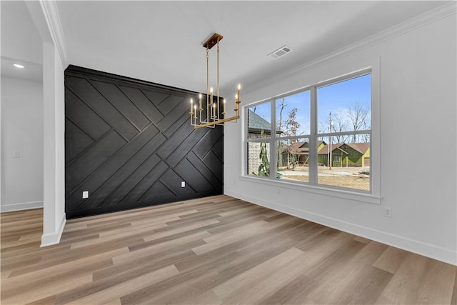 unfurnished dining area with wood finished floors, visible vents, an inviting chandelier, ornamental molding, and an accent wall