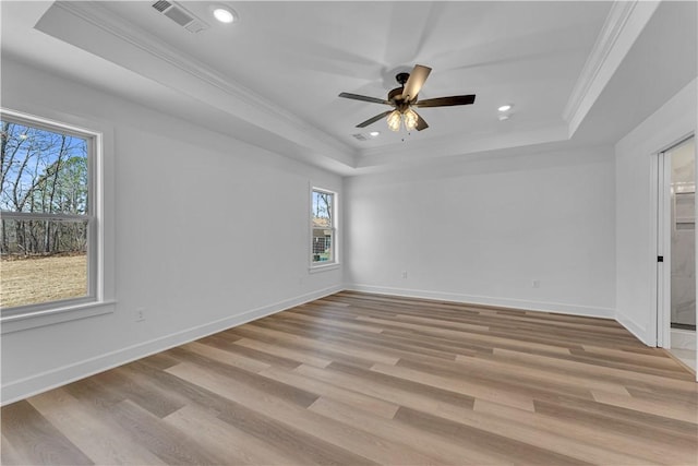 empty room featuring visible vents, ornamental molding, light wood-style flooring, a tray ceiling, and baseboards