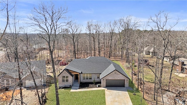 view of front of home with a front lawn, driveway, a wooded view, a garage, and brick siding