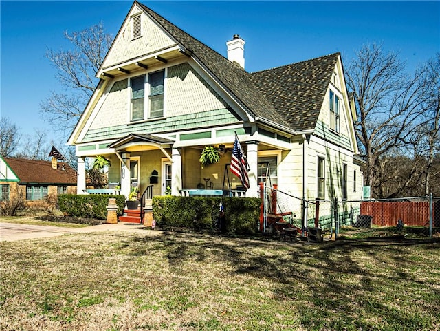 victorian home with a front lawn, covered porch, a chimney, and fence