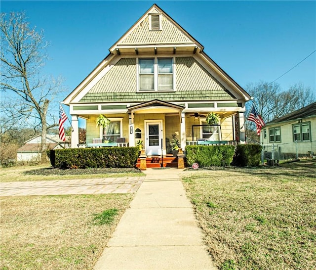 victorian house with a porch, a front yard, and fence