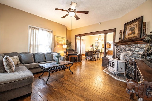 living area with hardwood / wood-style floors, a wood stove, ceiling fan with notable chandelier, and a textured ceiling