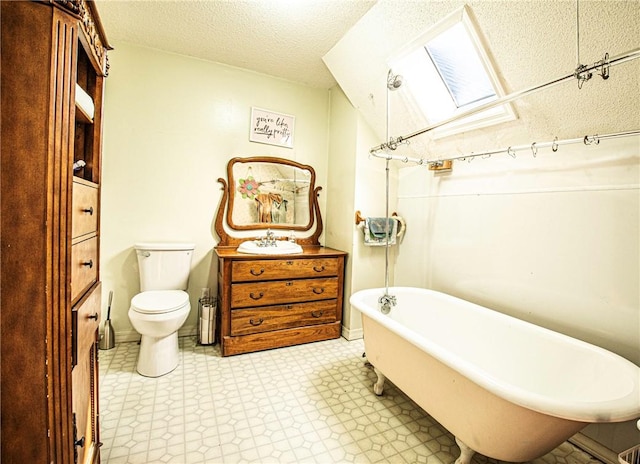 bathroom featuring toilet, vanity, a skylight, a freestanding tub, and a textured ceiling