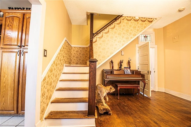 stairs with wallpapered walls, wood finished floors, baseboards, and a textured ceiling