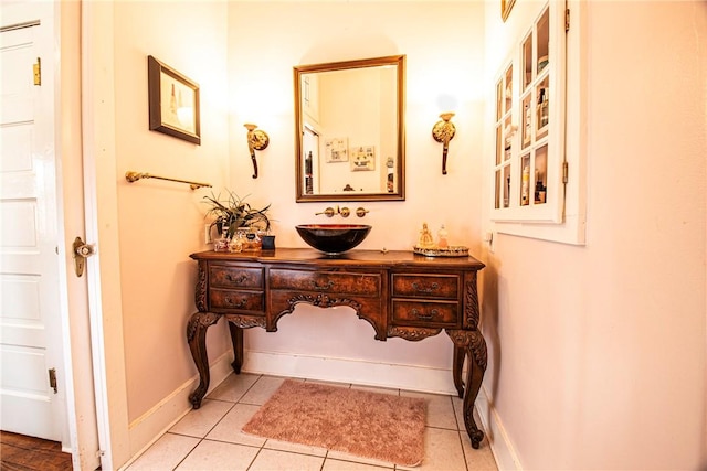 corridor featuring light tile patterned floors, baseboards, and a sink