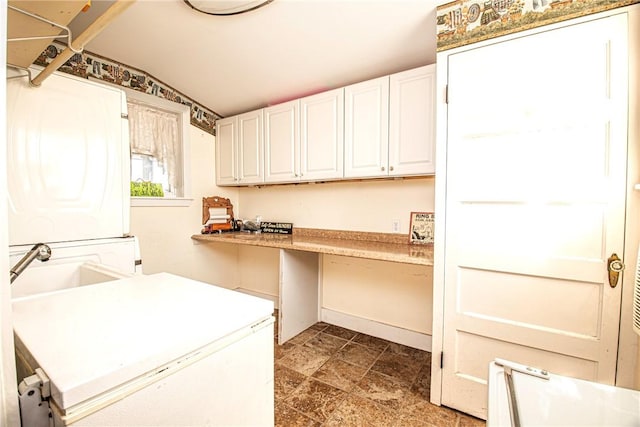 clothes washing area featuring a sink, cabinet space, stone finish floor, and stacked washer and dryer