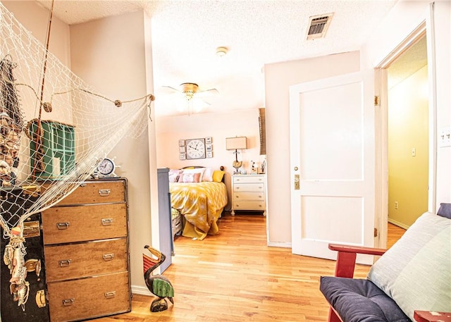 bedroom with baseboards, light wood-style floors, visible vents, and a textured ceiling