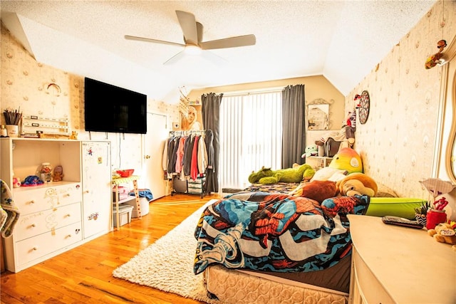 bedroom featuring a textured ceiling, wallpapered walls, lofted ceiling, and wood finished floors