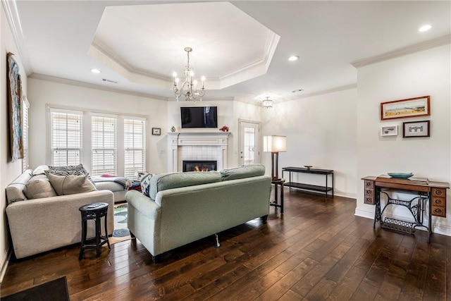 living room featuring baseboards, a tray ceiling, a tile fireplace, dark wood-style floors, and a notable chandelier