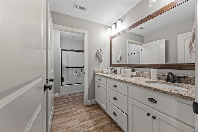 bathroom with wood finish floors, combined bath / shower with glass door, visible vents, and a sink