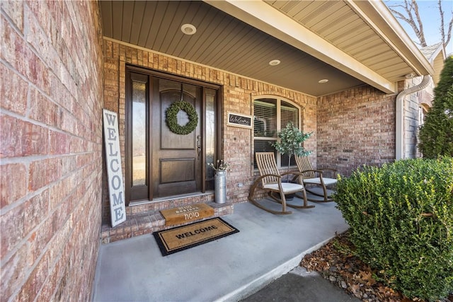 view of exterior entry with a porch and brick siding