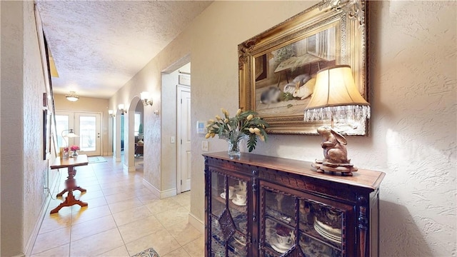 corridor with light tile patterned floors, arched walkways, a textured ceiling, and a textured wall