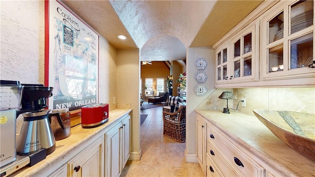 kitchen featuring a textured ceiling, backsplash, light countertops, light tile patterned floors, and glass insert cabinets