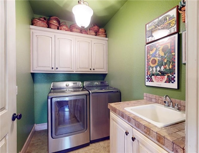 laundry room with a sink, cabinet space, light tile patterned flooring, baseboards, and washing machine and clothes dryer