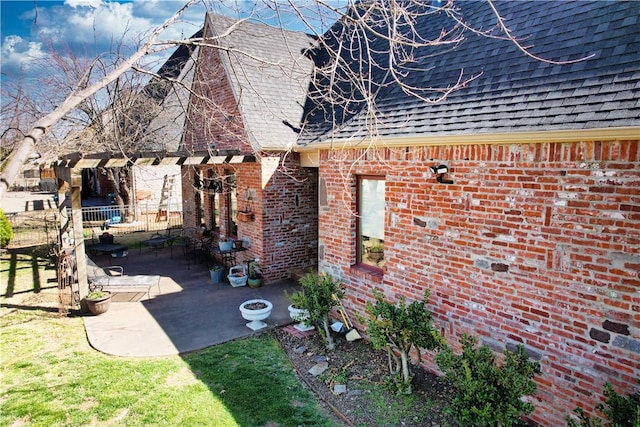 view of side of home with a patio, brick siding, roof with shingles, and fence