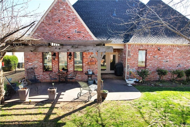 view of front of property with a shingled roof, a front lawn, french doors, a patio area, and brick siding