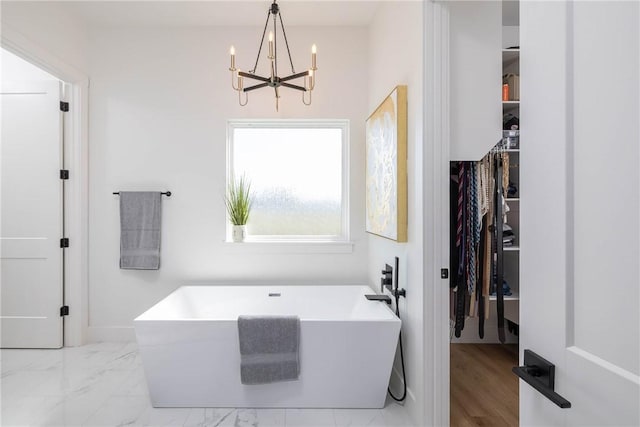 full bathroom with a walk in closet, marble finish floor, a chandelier, and a freestanding bath