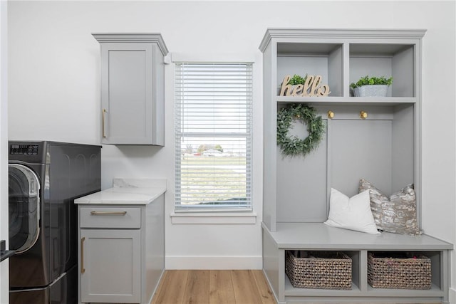 laundry area featuring baseboards, cabinet space, washer / dryer, and light wood-style flooring