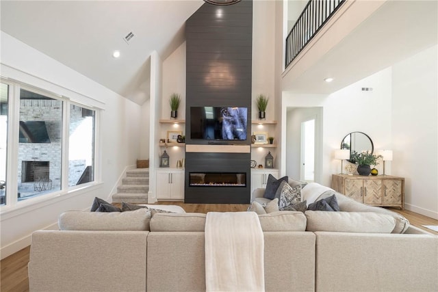 living room featuring baseboards, wood finished floors, visible vents, and a glass covered fireplace