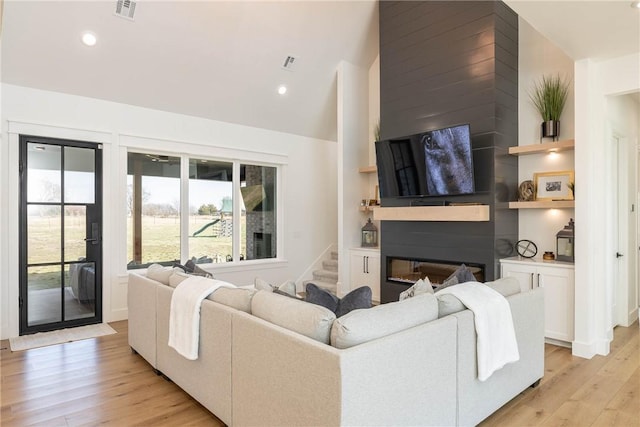 living area with a glass covered fireplace, built in shelves, light wood-style floors, and visible vents