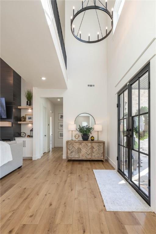 foyer featuring visible vents, baseboards, light wood-style flooring, a towering ceiling, and a notable chandelier