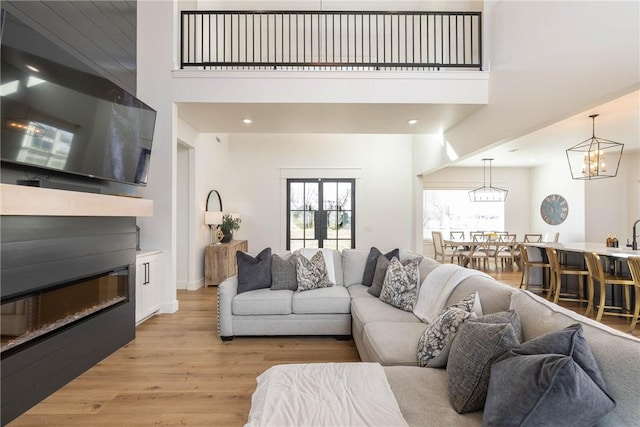 living area with a chandelier, recessed lighting, light wood finished floors, and a towering ceiling