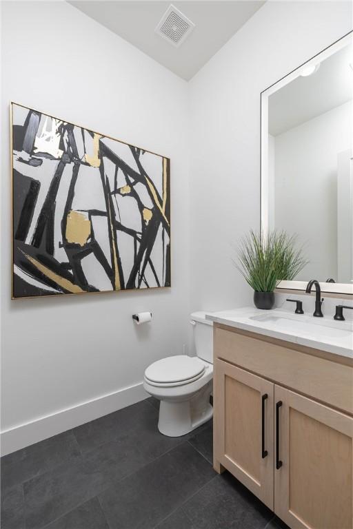 half bathroom featuring vanity, baseboards, visible vents, tile patterned floors, and toilet