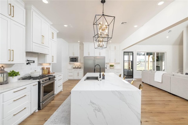 kitchen with light wood-style flooring, a sink, open floor plan, built in appliances, and a chandelier