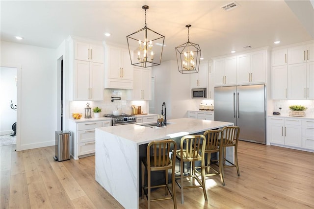 kitchen with light wood finished floors, visible vents, high quality appliances, an inviting chandelier, and a sink