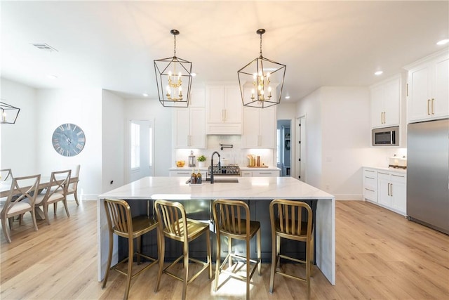 kitchen featuring light wood finished floors, a center island with sink, recessed lighting, an inviting chandelier, and stainless steel appliances