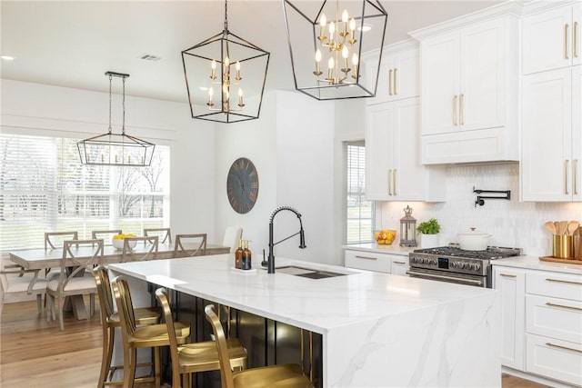 kitchen featuring a notable chandelier, a kitchen island with sink, a sink, high end stainless steel range oven, and decorative backsplash