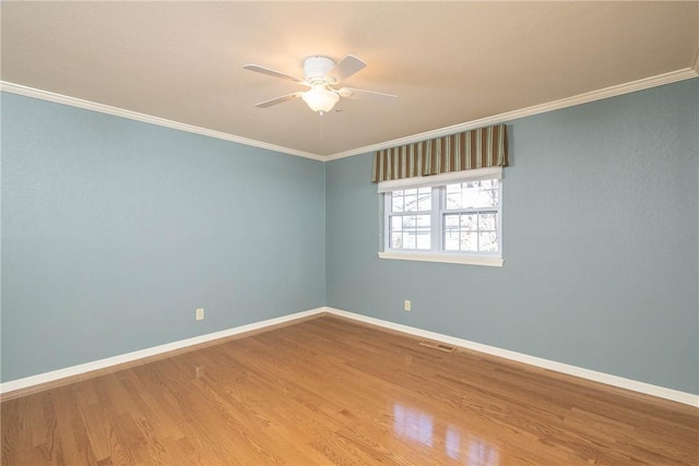 empty room with a ceiling fan, crown molding, wood finished floors, and baseboards