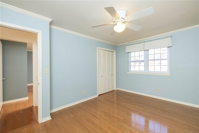 unfurnished bedroom featuring crown molding, wood finished floors, a closet, and baseboards