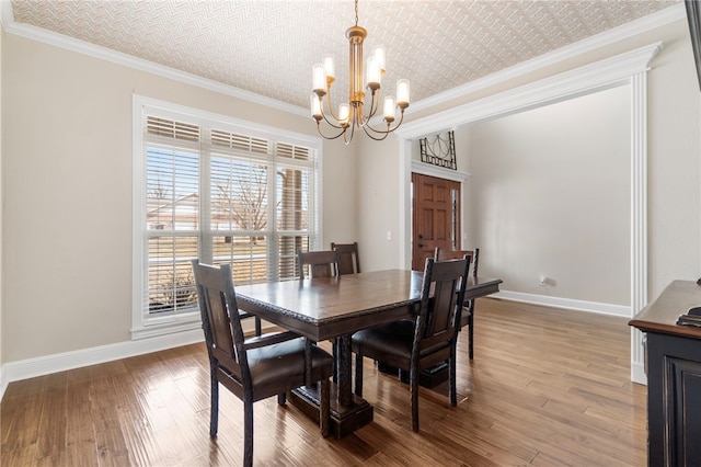 dining room with ornamental molding, wood finished floors, baseboards, and a chandelier