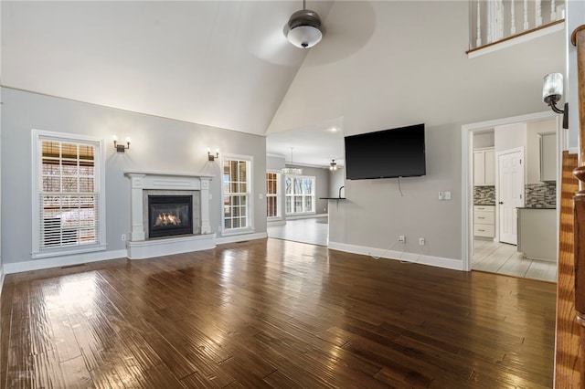 unfurnished living room with high vaulted ceiling, a ceiling fan, a glass covered fireplace, wood-type flooring, and baseboards