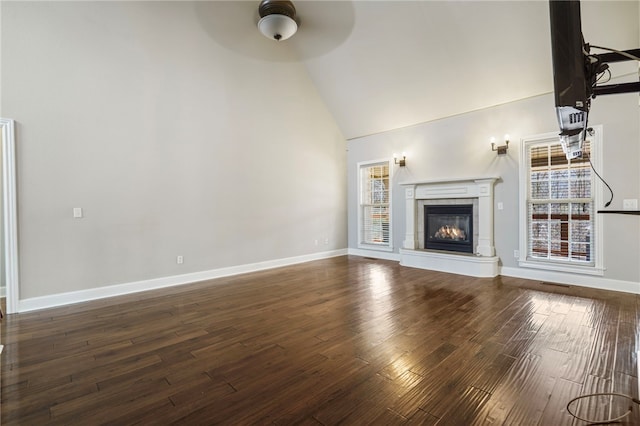 unfurnished living room featuring a ceiling fan, baseboards, high vaulted ceiling, dark wood finished floors, and a glass covered fireplace