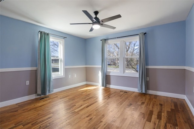 spare room featuring visible vents, a ceiling fan, baseboards, and wood finished floors