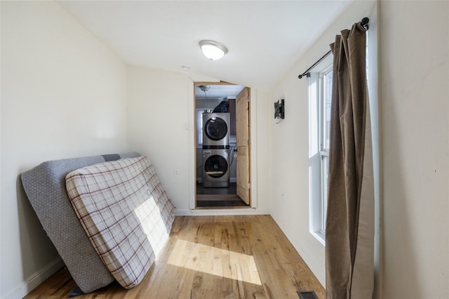 interior space with visible vents, baseboards, stacked washer and dryer, and wood finished floors