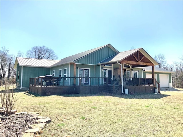 rear view of property with a porch, an attached garage, a lawn, and metal roof