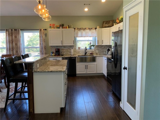 kitchen with visible vents, a kitchen bar, white cabinets, black appliances, and a sink