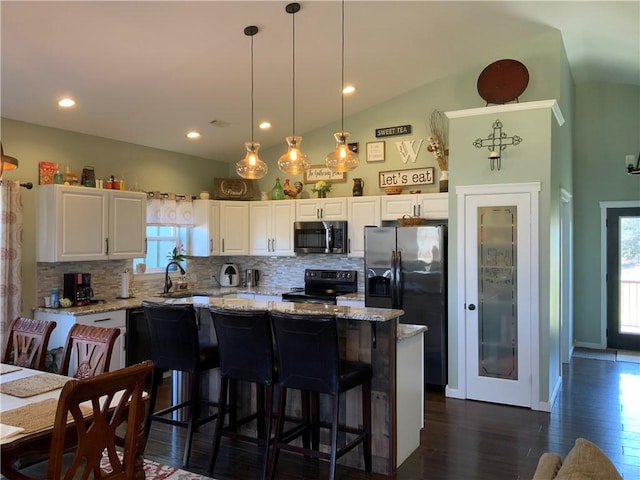 kitchen with light stone counters, backsplash, white cabinetry, appliances with stainless steel finishes, and vaulted ceiling