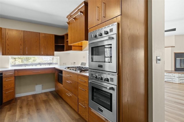 kitchen with wood finished floors, open shelves, brown cabinetry, and appliances with stainless steel finishes