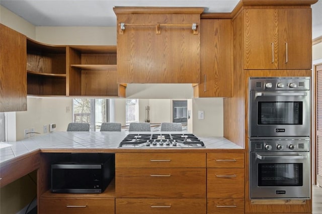 kitchen with tile countertops, appliances with stainless steel finishes, brown cabinets, and open shelves