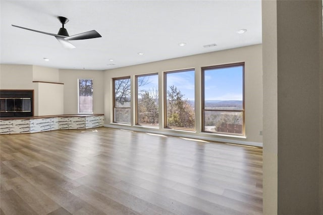 unfurnished living room featuring recessed lighting, a premium fireplace, wood finished floors, and a ceiling fan