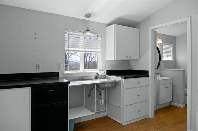 kitchen featuring light wood-type flooring, dark countertops, white cabinetry, vaulted ceiling, and hanging light fixtures