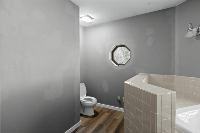 full bathroom featuring a garden tub, baseboards, toilet, and wood finished floors