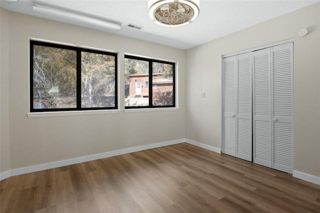 unfurnished bedroom with a closet, visible vents, baseboards, and wood finished floors