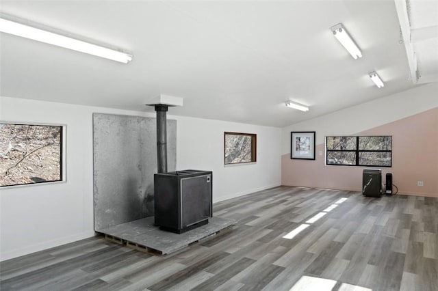 unfurnished living room with wood finished floors, a wood stove, baseboards, and vaulted ceiling